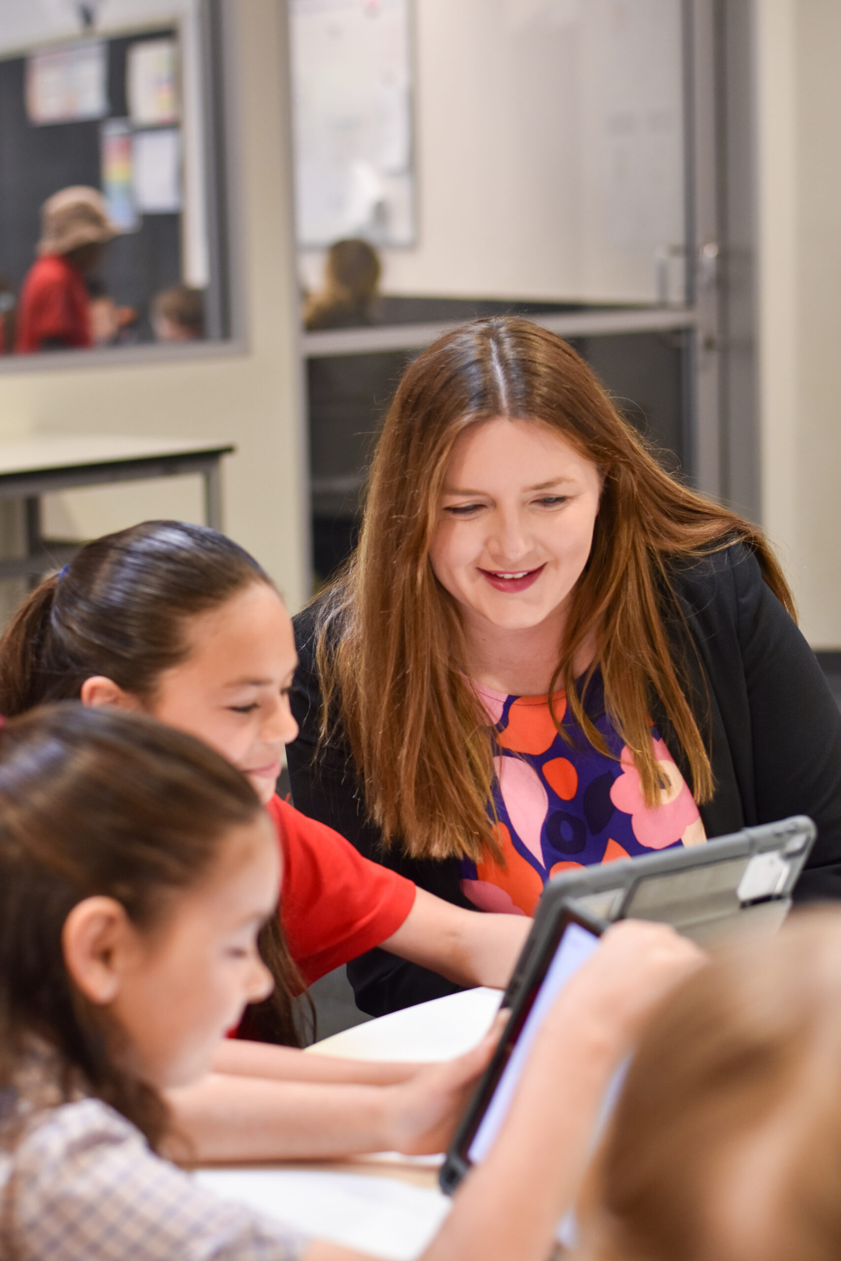Teacher working with two primary students on a tablet in the classroom