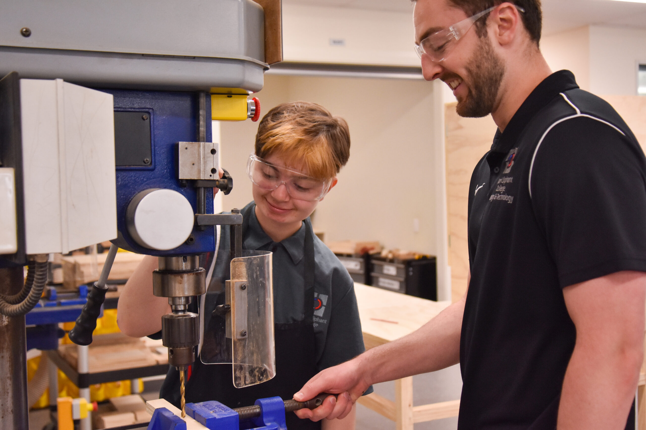 Student using a drill press in design and technology while a teacher supervises