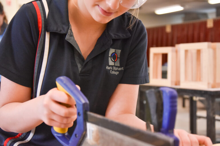 Student using a hand saw at a workbench in the technologies workshop