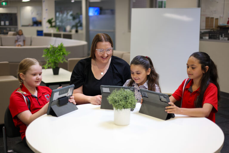 Teacher working with primary students using iPads at a table