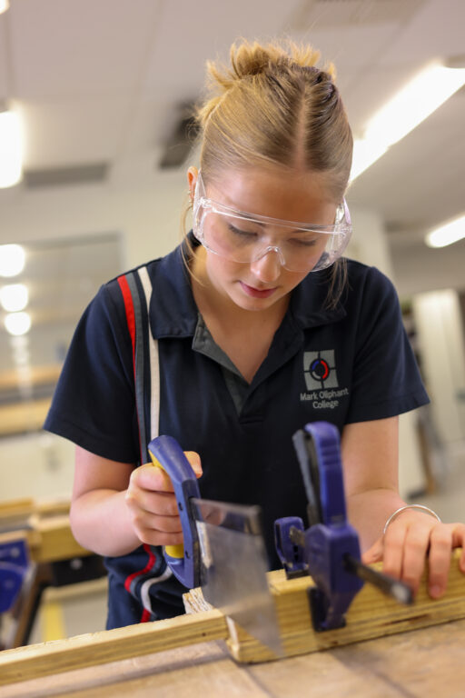 Student in safety glasses working with tools at a workbench