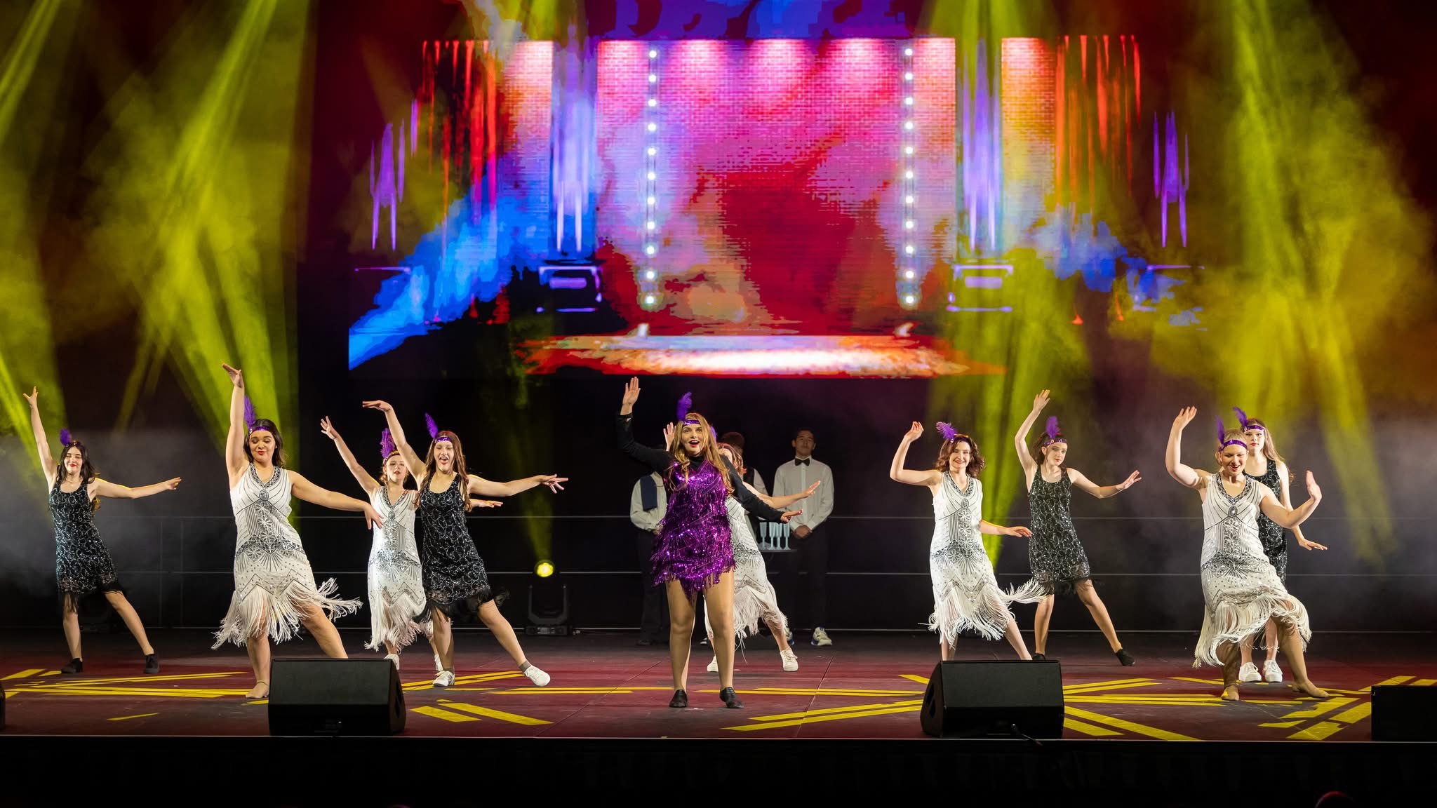 Students performing on stage in 1920s-style costumes under stage lighting