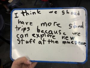 Student whiteboard reading 'I think we should have more school trips because we can explore new stuff at the museum'