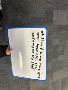 Student whiteboard reading 'We should have more iPad time because I like learning on my iPad'