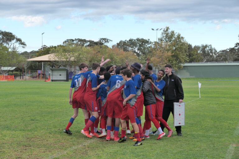 Year 9/10 boys knockout soccer team celebrating in a group huddle