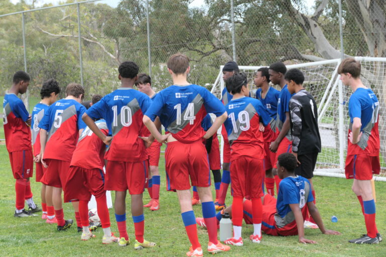 Year 9/10 boys knockout soccer team gathered with their coach beside the goal