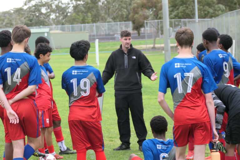 Coach speaking to the Year 9/10 boys knockout soccer team on the field