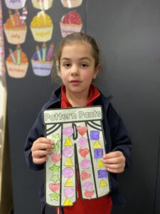 Year 1D student holding their Pattern Pants artwork decorated with pink and green hearts
